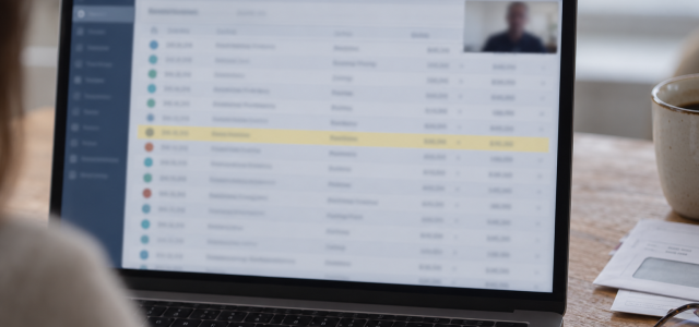 A laptop on a kitchen table showing a blurred list of transactions with one row highlighted
